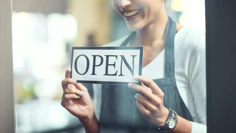 Shot of a young woman hanging an open sign on the door of her store