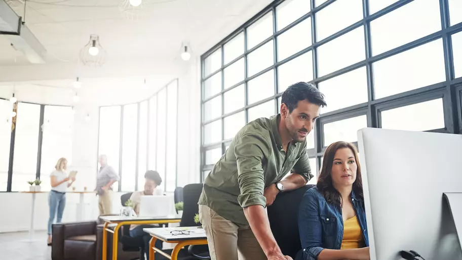 a woman sitting at a computer talking to the man standing behind her