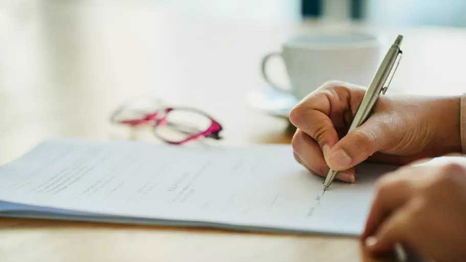 A silver pen writing with glasses in the background