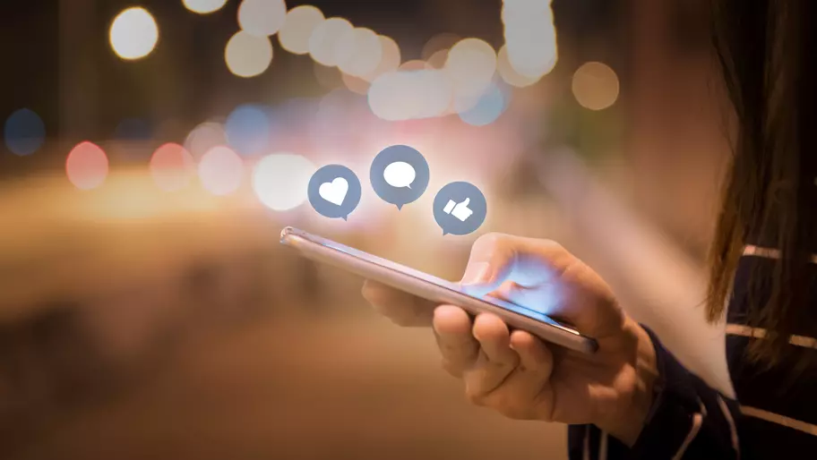 Hand holding smart phone and social media icons.