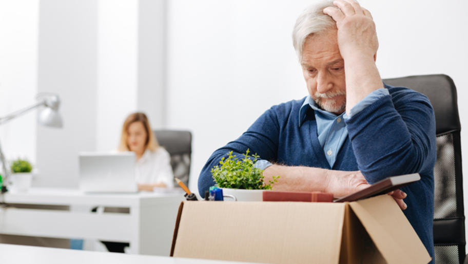 Middle-aged man looking distressed at work, hunched over cardboard box with his desk items