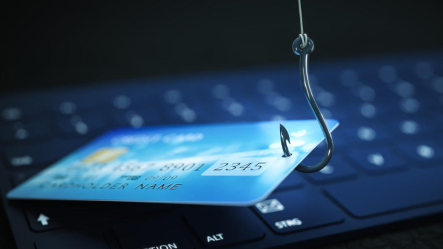 Credit card on fishing hook being lifted from on top of a computer keyboard. Phishing cyber attack.