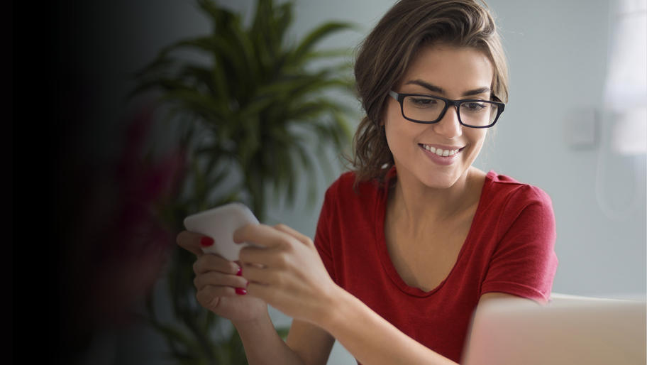 Young, female small business owner wearing red shirt and holding a smart phone.