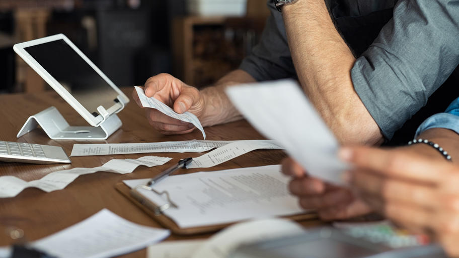 Image of man's and woman's hands on table holding receipts and doing business taxes