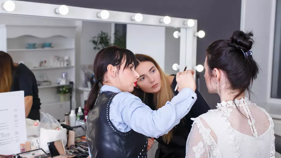 Two women practicing cosmetology/makeup techniques on model. 