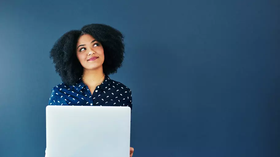 Woman standing in front of blue background holding laptop. Social media for businesses.