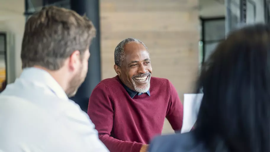 Three people sitting around a conference table. One man smiling.