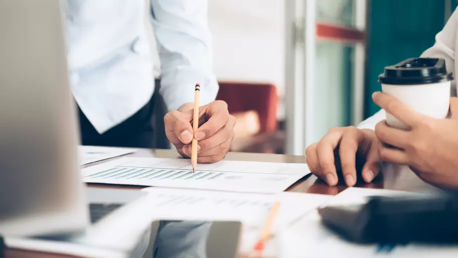 Image of men's hands on desk with papers, pencil, and laptop