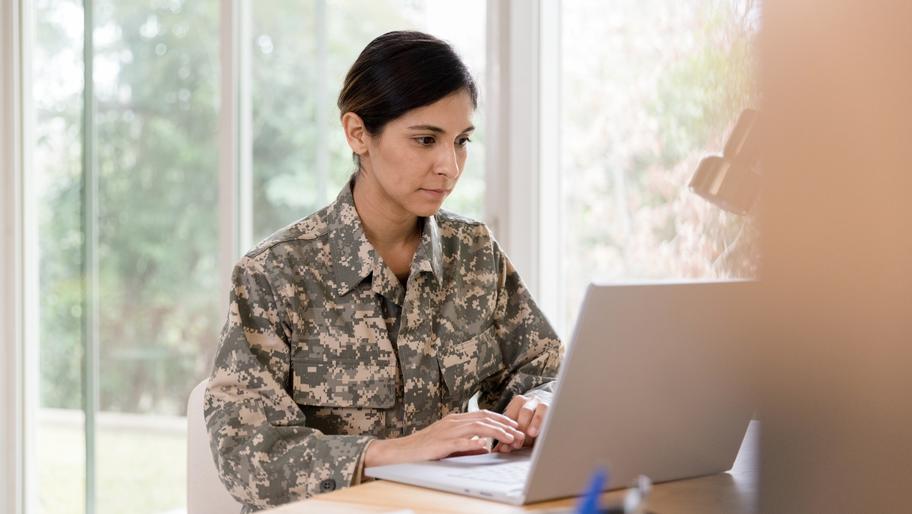 Veteran, woman, sitting at desk on laptop. Veteran small business owner.