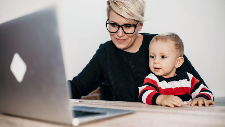 mom entrepreneur sitting at computer, working with her young child on her lap
