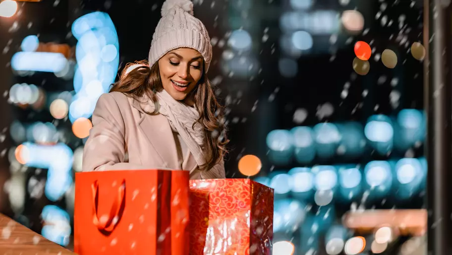 small business owner outside in snow with red gift bags excited for holiday shopping season