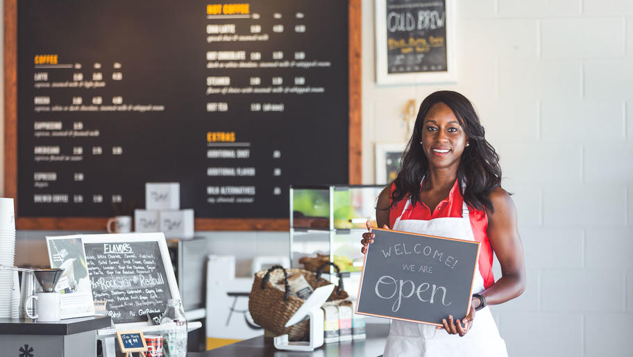 female small business owner with "welcome we're open" sign
