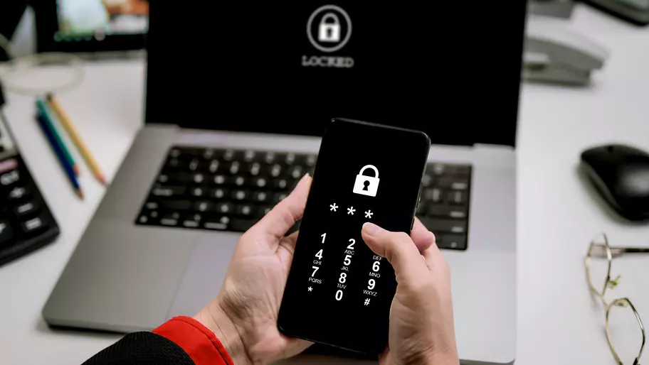open laptop on desk while hands wrap around cellphone, using multifactor security to login
