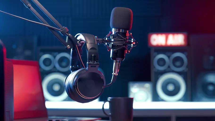 setting for podcast taping, microphones and 'on air' sign in the background. Darker colors with a pop of red in the left corner