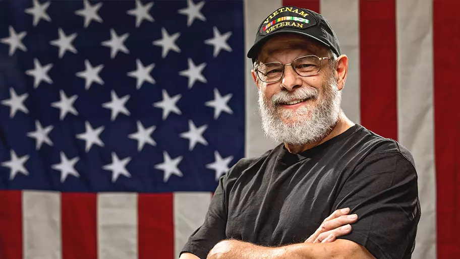 Vietnam veteran standing in front of the American flag with arms crossed