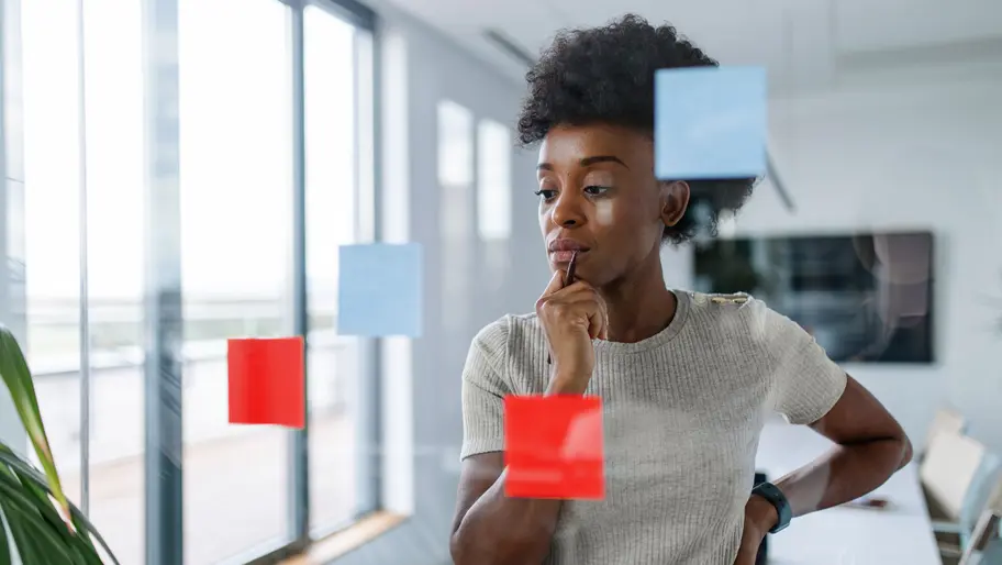 Entrepreneur looking at clear memo board with red post-its trying to figure out his next steps.