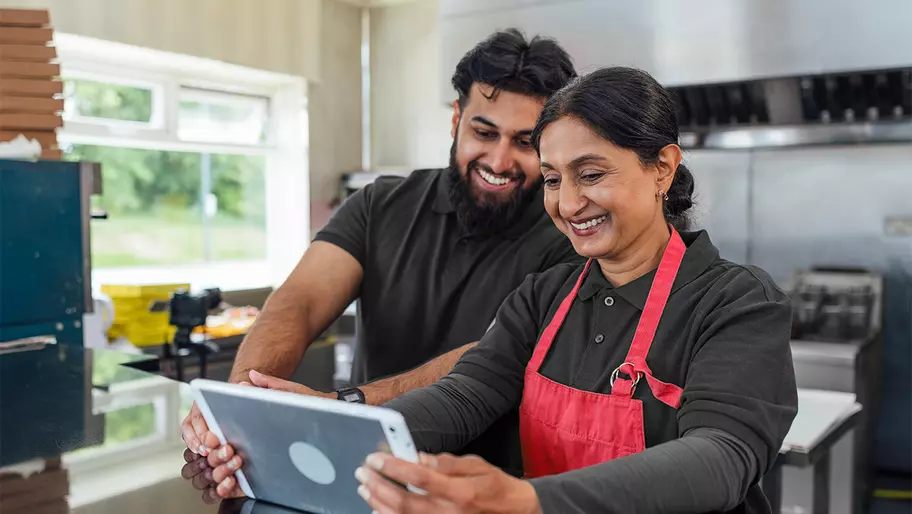 male and female business owners looking at a mobile device, happily, in their mom and pop shop