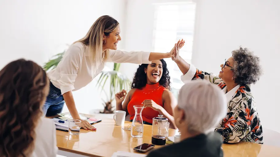 office with white walls, five excited business women high-fiving for amber grants