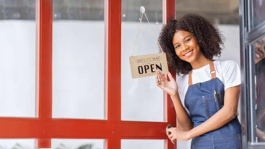 Happy Black female entrepreneur owner standing in front of her small business