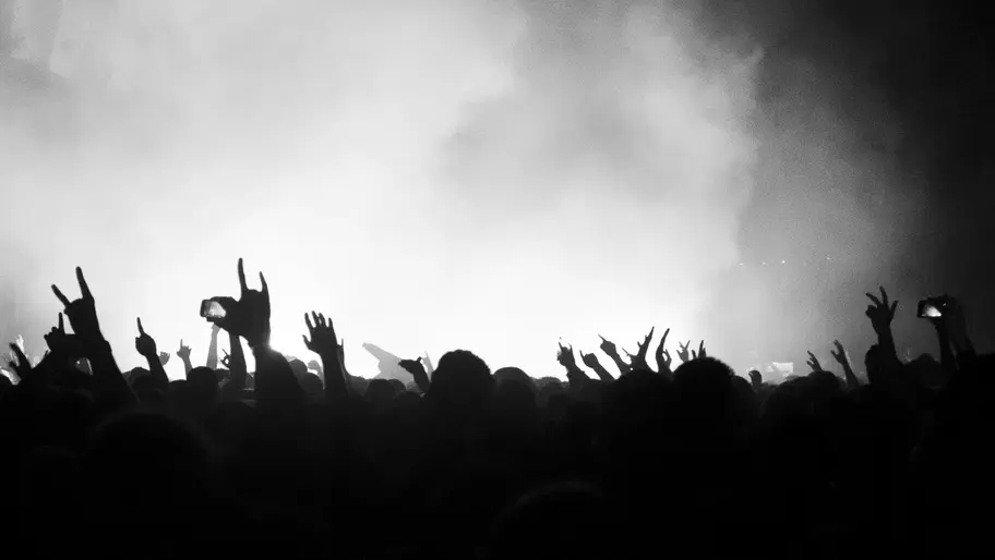 Black and white image of fans attending heavy metal concert, holding sign of the horns hands high in the air.