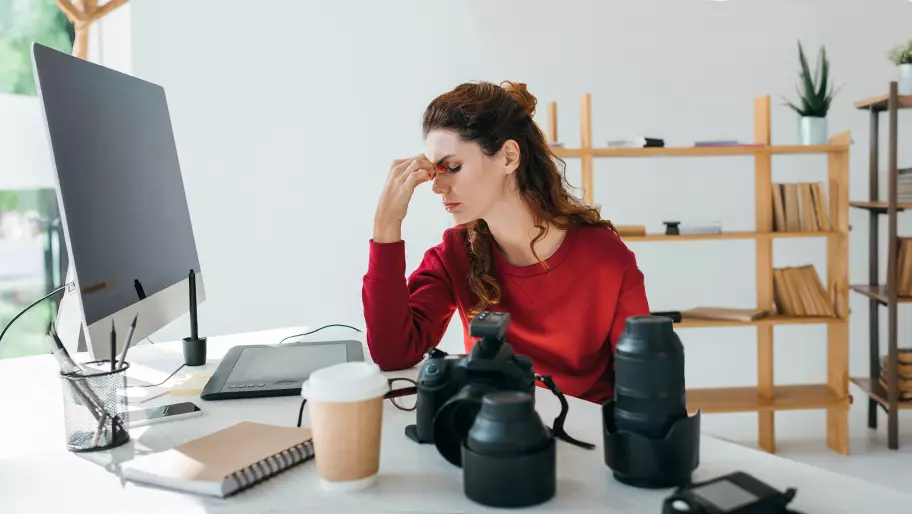 stressed female photographer sitting at desk with tension building trying to handle multiple projects.