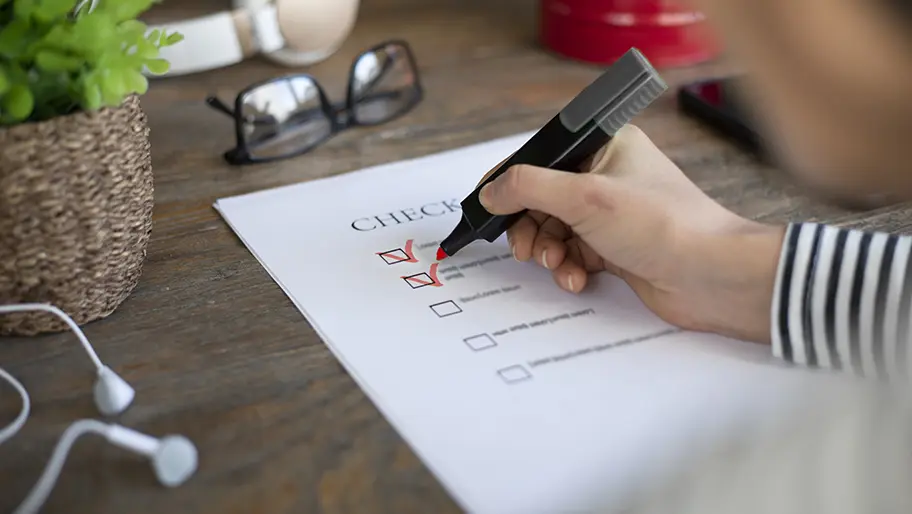 Checklist on a business owner's desk with hand checking items off with pen.