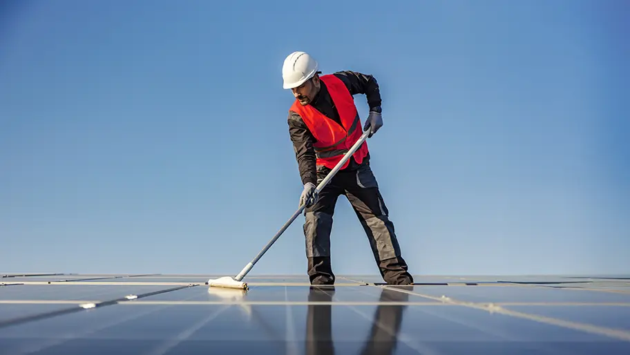 Cleaning business worker using a long‑handled tool to wash a rooftop under a clear blue sky.