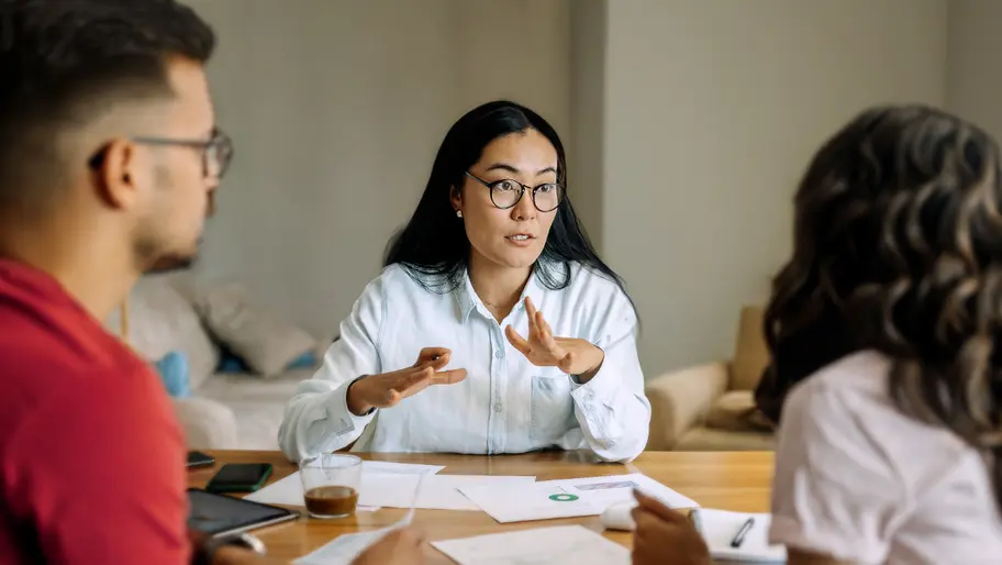 Life coach leading a coaching session with two clients at a table, discussing plans and reviewing documents during a one-on-one meeting.