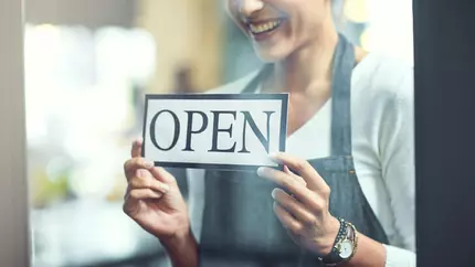 Shot of a young woman hanging an open sign on the door of her store