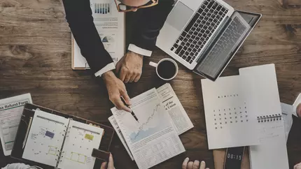 Man's hands on desk pointing to a chart with a pen