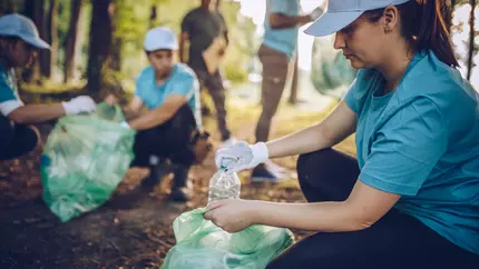 Men and women picking up trash in the woods and recycling it
