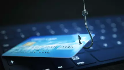 Credit card on fishing hook being lifted from on top of a computer keyboard. Phishing cyber attack.