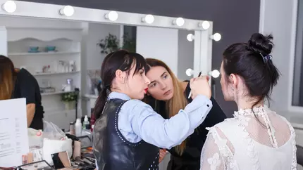 Two women practicing cosmetology/makeup techniques on model. 