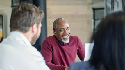 Three people sitting around a conference table. One man smiling.