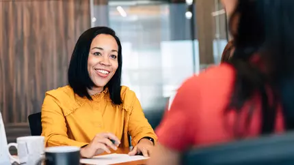 Woman in yellow shirt sitting across from her mentee and smiling.