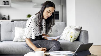 Woman sitting on couch working with paperwork and tablet. How to apply for business insurance.
