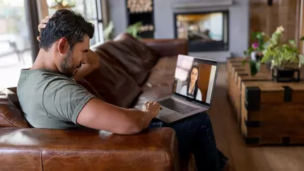 Man sits on couch with telehealth professional on laptop