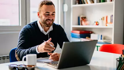 Employee for small business sitting at desk in home office working remotely with laptop in front of him