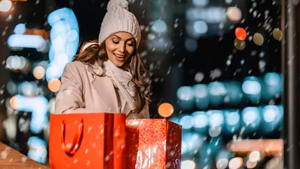 small business owner outside in snow with red gift bags excited for holiday shopping season