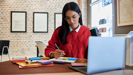 Woman in red sweater sitting with laptop reviewing small business insurance coverage