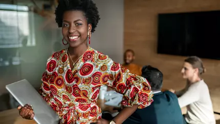 Black woman entrepreneur standing proud with smile on her face. Office environment in the background.