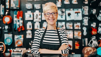 Female small business owner with glasses in black and white striped shirt standing behind a counter