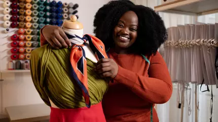 Black woman with mannequin working on alterations in her tailor shop