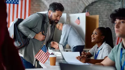 male business owner waiting to vote in US presidential election. US flag in the background