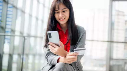 Female business owner sitting outside on mobile phone with credit card in-hand buying business insurance