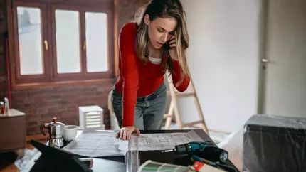 female interior decorator standing over desk looking at swatches, on phone with client