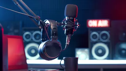 setting for podcast taping, microphones and 'on air' sign in the background. Darker colors with a pop of red in the left corner
