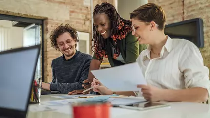 Three happy business owners smiling at desk discussing beneficial owner registration information