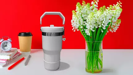 Red background with white Stanley style tumber sitting next to flowers on a table