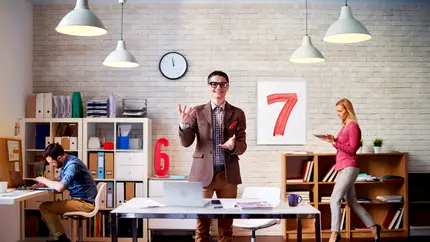 Modern office with three people working, featuring large red numbers 6 and 7 on the wall.